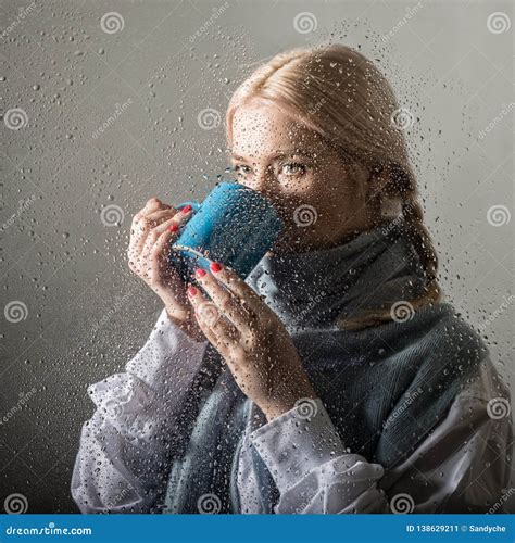 Young Blonde Woman Behind Glass With Water Drops Beautiful Girl Drinks