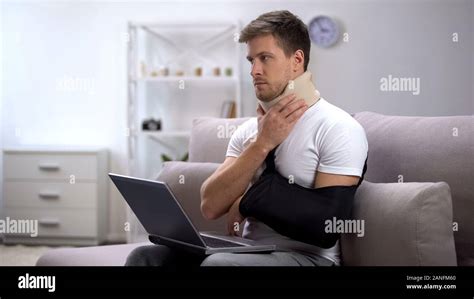 Injured Man In Foam Cervical Collar And Arm Sling Working On Laptop