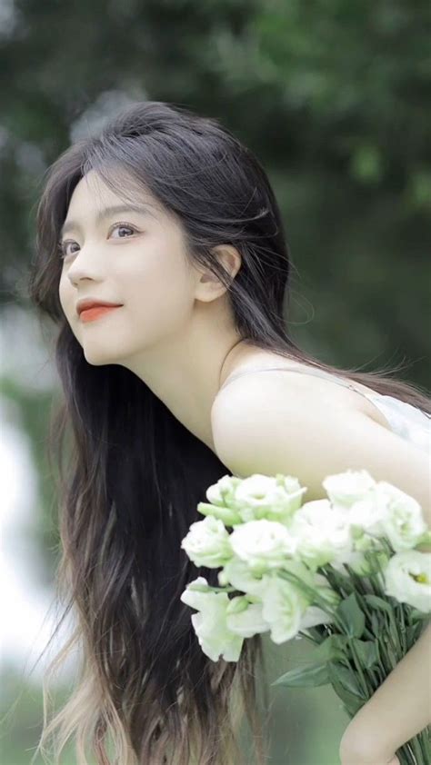 A Woman With Long Black Hair Holding A Bouquet Of White Flowers In Her