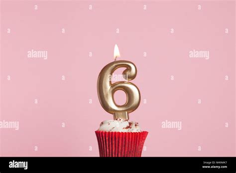 Number 6 gold candle in a cupcake against a pastel pink background ...