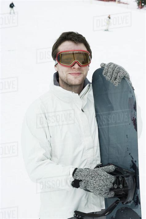 Young man standing with snowboard, portrait - Stock Photo - Dissolve