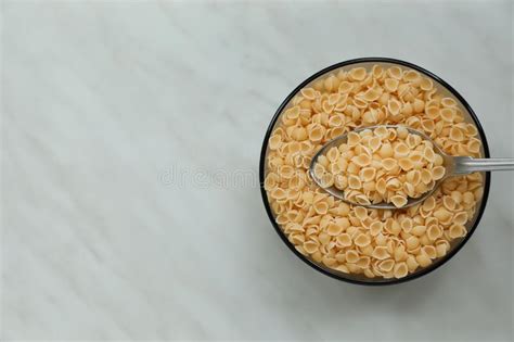 Bowl Of Uncooked Conchiglie Pasta And Spoon On White Marble Table Top