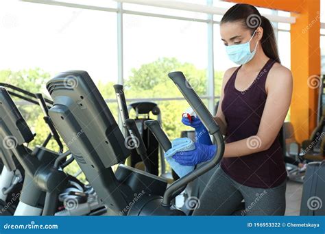 Woman Cleaning Exercise Equipment With Disinfectant Spray And Cloth In