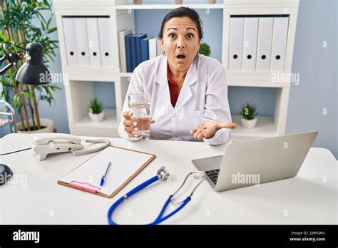 Hispanic Mature Doctor Woman Holding Pill And Glass Of Water Afraid And
