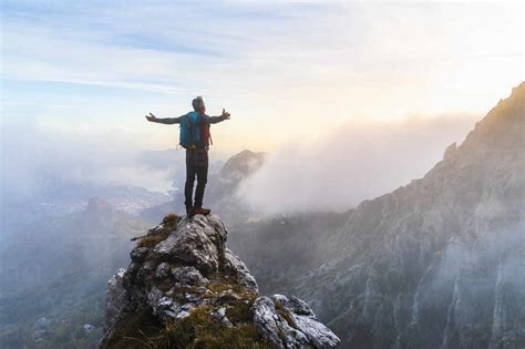 Pensive Hiker With Arms Outstretched Standing On Mountain Peak During