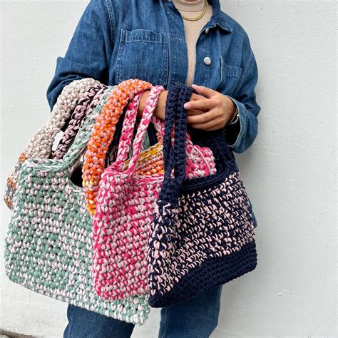 A Woman Is Holding Several Crocheted Purses In Her Hands And Standing