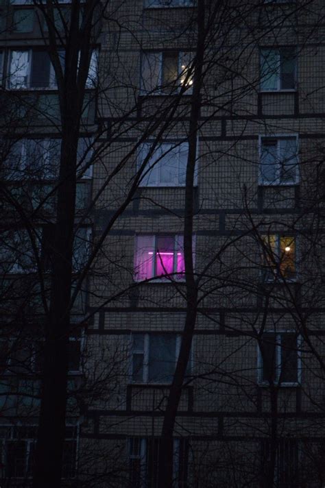 An Apartment Building Is Lit Up With Pink Light In The Window And Trees