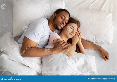 Loving Multiracial Couple Having Cozy Morning Cuddling Together In Their Sleep On Bed Top View