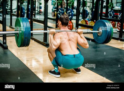 Man in squatting position weightlifting at gym Stock Photo - Alamy