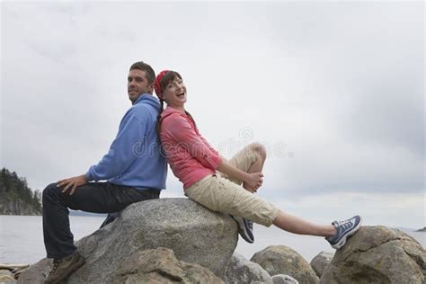 Couple Sitting Back To Back On Rocks Against Ocean Stock Photo Image