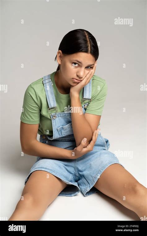 Boring Brunette Tan Teen Girl Sitting On Gray Background Looking At Camera Resting Cheek On Hand