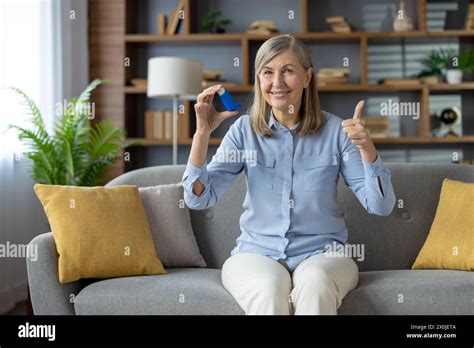 A Positive Mature Woman Comfortably Sitting On A Sofa At Home Uses An Asthma Inhaler She Gives