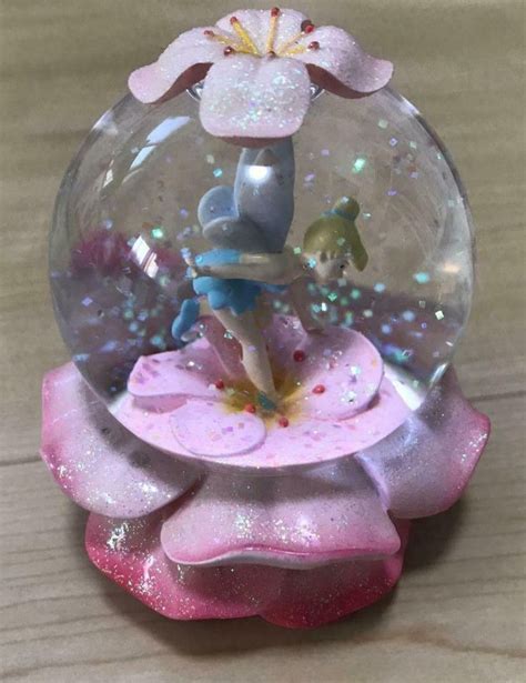 A Snow Globe With A Pink Flower Inside On A Wooden Table Next To A