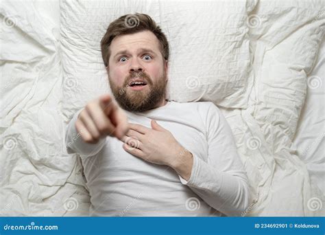 Frightened Man Lies In Bed Pointing Up And Holds Hand On Chest He Is