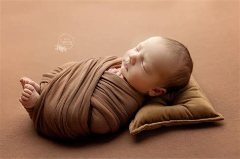 A Baby Wrapped In A Brown Wrap Sleeping On A Pillow With His Head Tucked Up