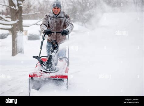 Man Using Snowblower To Clear Deep Snow On Residential Driveway After