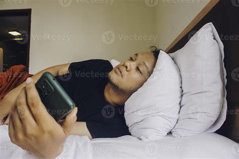 Tired Young Man Checking On His Phone While Lying In Bed 12705750 Stock