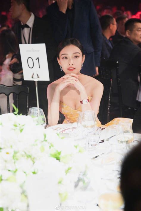 A Woman Sitting At A Table With Flowers In Front Of Her And A Sign That