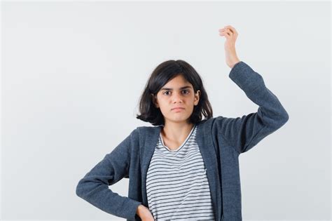 Petite fille levant la main en t shirt veste et à la confusion Photo