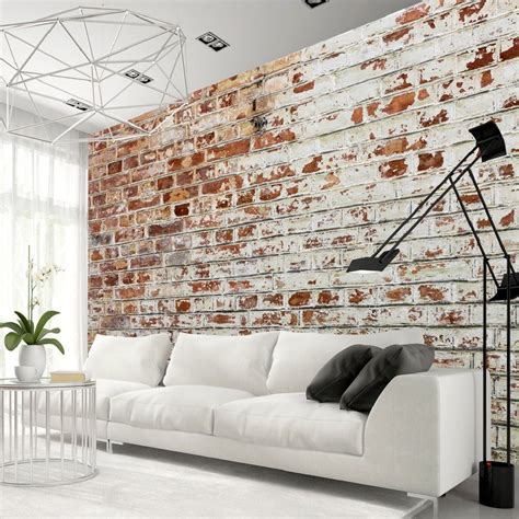 A White Couch Sitting In Front Of A Brick Wall Next To A Table And Chair