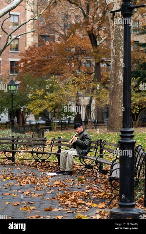 An Older Man Sitting On A Park Bench Playing The Trumpet In The Fall