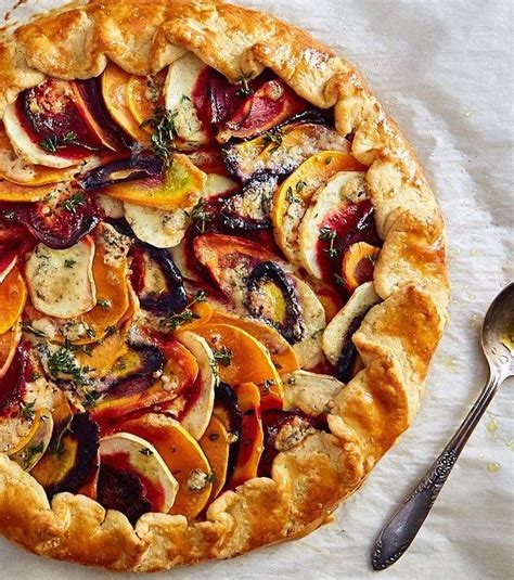 A Pie With Fruit And Herbs On It Sitting Next To A Silver Spoon Fork