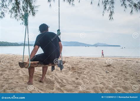 A Man Sitting On Wooden Swing On The Layan Beach In Phuket Thai