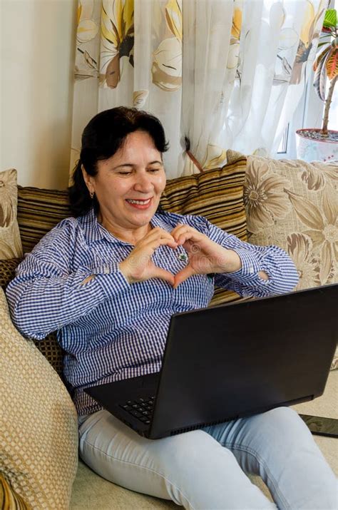 Charming Mature Woman Chatting Online Using Laptop Webcam While Sitting On Sofa In Living Room