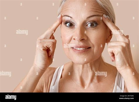Sporty Mature Woman Doing Face Building Exercise On Beige Background