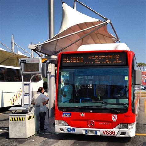 A Red And White Bus Parked At A Bus Stop Next To A Man Standing In