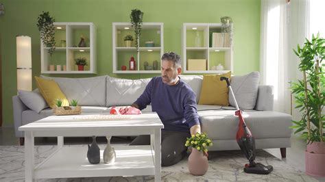 An Elderly Man Wipes Dust From Furniture For Hygiene In The Living Room