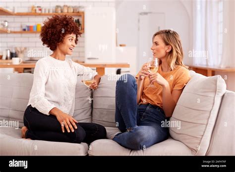 Two Female Friends Relaxing On Sofa At Home With Glass Of Wine Talking