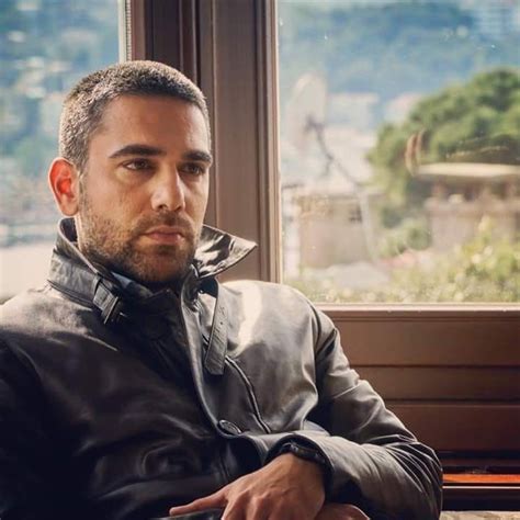 A Man Sitting In Front Of A Window Wearing A Leather Jacket