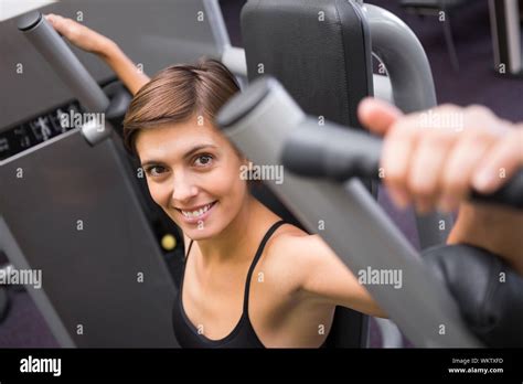 Happy Brunette Using Weights Machine For Arms At The Gym Stock Photo