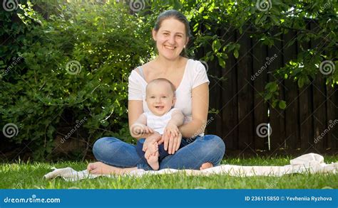 Cute Baby Boy Sitting On Mothers Lap In Park And Smiling In Camera