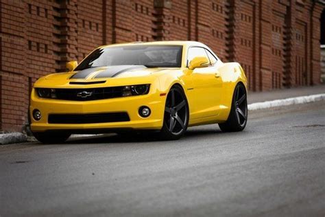 A Yellow Chevrolet Camaro Parked On The Side Of A Road Next To A Brick Wall