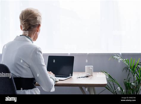 Back View Of Senior Businesswoman Using Laptop With Blank Screen In