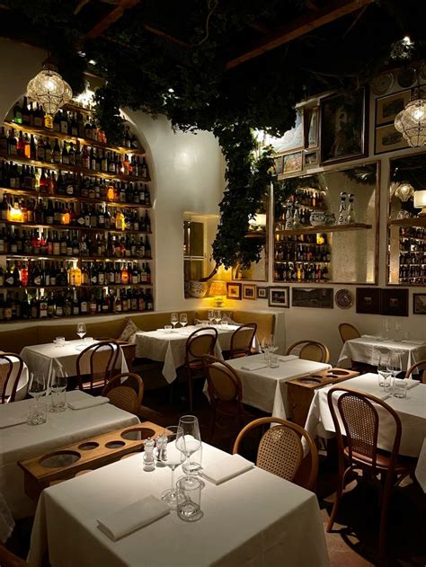 A Dimly Lit Dining Room With Many Bottles On The Wall And Tables Set