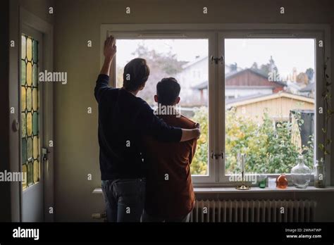Rear View Of Man With Arm Around Gay Couple Looking Through Window At