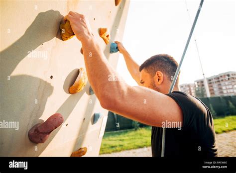 Man Wearing Belaying Rope Climbing On A Very High Rock Climbing Wall