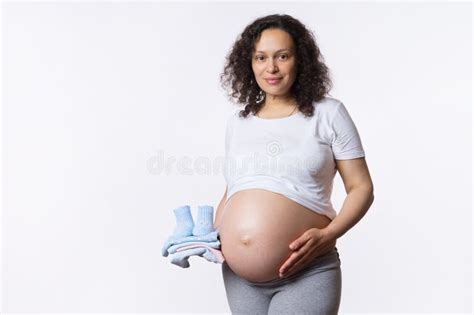 Beautiful Latina Pregnant Woman Smiling At Camera Touching Her Big Belly Holding Baby Clothes