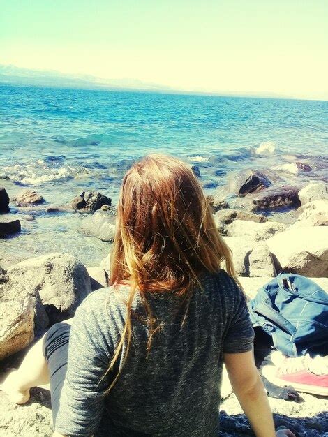 Premium Photo Rear View Of Woman Sitting On Rocks At Beach