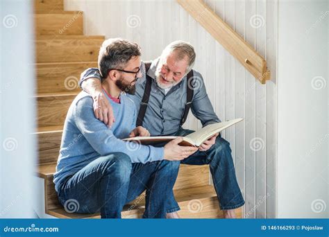 An Adult Son And Senior Father Sitting On Stairs Indoors At Home