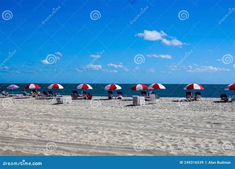 A Row Of Red And White Striped Umbrellas Are Seen Along The Beach By