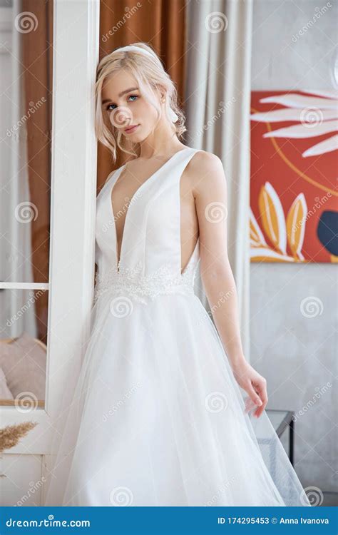 Beautiful Slender Blonde In The Evening Sun In A Long White Dress Near A Large Window Perfect