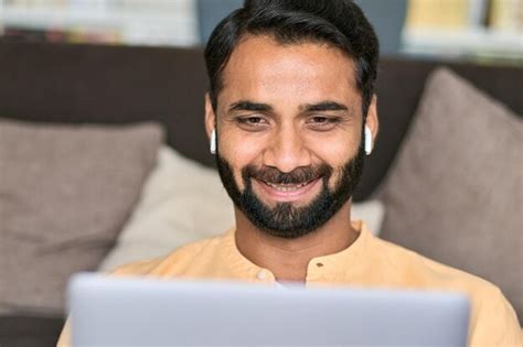 Homem Indiano Sorridente Sentado Em Casa Usando Fones De Ouvido Usando