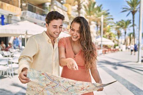 Pareja De Hombres Y Mujeres Sonriendo Confiados Sosteniendo Un Mapa En