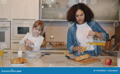 Niñita Llenando El Plato Con Cereal Mientras La Niñera Vierte Jugo En