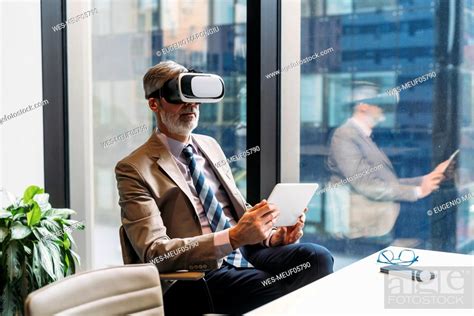 Mature Businessman Wearing Virtual Reality Simulator Sitting With