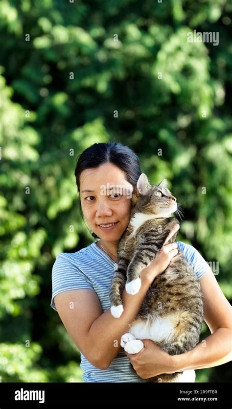Mature Woman Holding Her Pet Cat While Outdoors During A Lovely Summer Day With Trees In